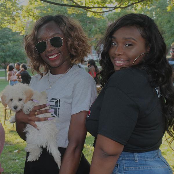 Two girls on the quad holding a puppy.